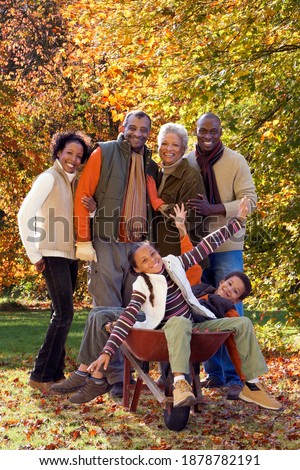Three generations of an African family are posing for a family picture on a sunny Autumn day with the kids are sitting in a wheelbarrow while the elders are standing behind them.
