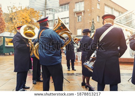 Street artists band plays wind instruments, trumpets and drums for audience gathered on street, military marching band orchestra playing in public square on rainy day dressed in uniform in England