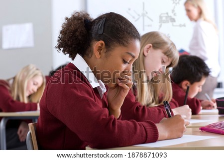 Sideview of students sitting in row with selective focus taking a test in the classroom while the supervisor is standing in background Royalty-Free Stock Photo #1878871093