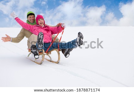 Happy adventurous couple sledding down a steep ski slope together legs up