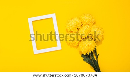 Bouquet of lush chrysanthemums and white picture frame lays on yellow background with copy space. Holiday or blank business card. Happy Valentine Day February 14. Woman Day March 8. Mother Day May 8.