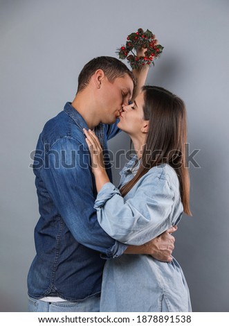 Happy couple kissing under mistletoe wreath on grey background
