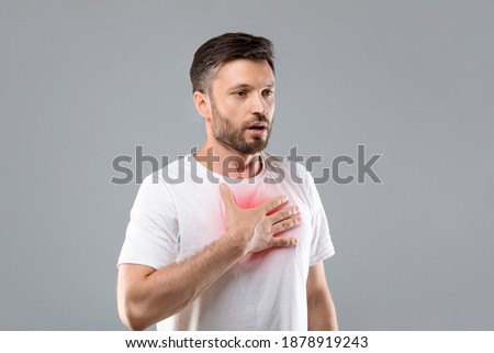 Breathing problem. Sick middle-aged man with chest pain touching inflammated zone and looking at copy space, grey studio background. Bearded man suffering from pneumonia or asthma. COVID-19 concept Royalty-Free Stock Photo #1878919243