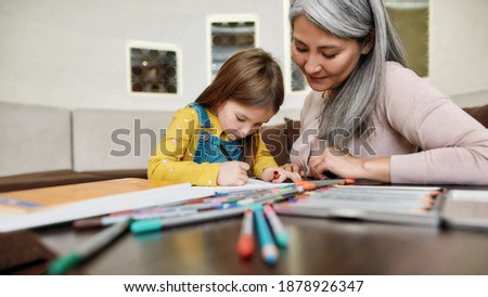 Little girl coloring picture in album during staying at home with grandmother, widescreen. Generation and happy family concept