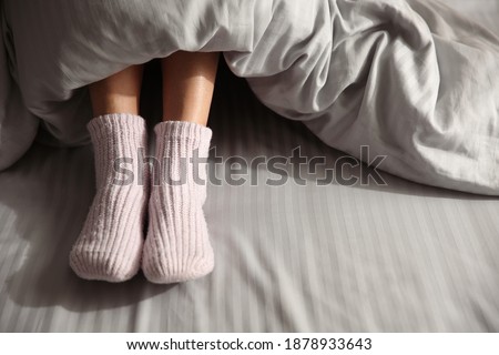 Woman wearing knitted socks under blanket in bed, closeup Royalty-Free Stock Photo #1878933643