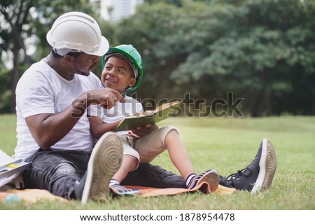 African engineer father and son spend time reading a book together at park, Father's day Royalty-Free Stock Photo #1878954478