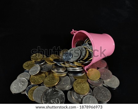 Selective focus.Picture of a Savings and Finance idea concept.Coins and pink bucket with black background.Shot were noise and film grain in full resolution.