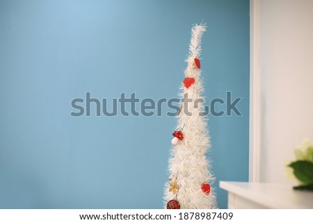 A white Christmas tree adorned against a mint-colored wall. A red Christmas sphere hangs as a point on an elongated tree.