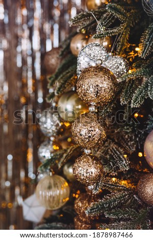 close-up of a Christmas tree with golden and silver toy balls and a garland. The foreground is in focus, the background is blurred