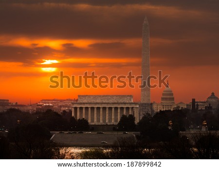 Bright orange sunlight illuminates clouds over Washington DC at dawn at sunrise. Lincoln, Washington Monument and Capitol are aligned