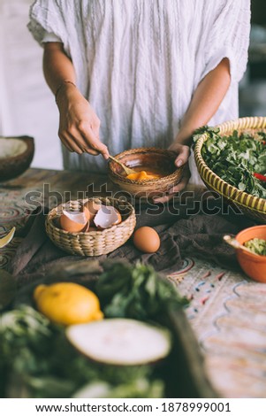 the process of making an omelet on a wooden table, there are ingredients around, hands beat eggs in a ceramic bowl