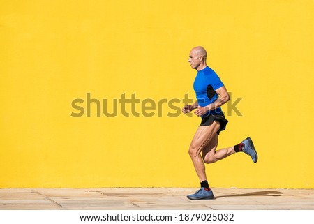 Photo with copy space of an sportsman with shaved head running in the street in front of a yellow wall