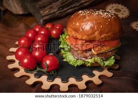 Commercial footage of fresh beef burger with a branch of fresh cherry tomatoes served on a decorative wooden part of a simple mechanism. Restaurant concept. Fast food concept. Street food concept. 