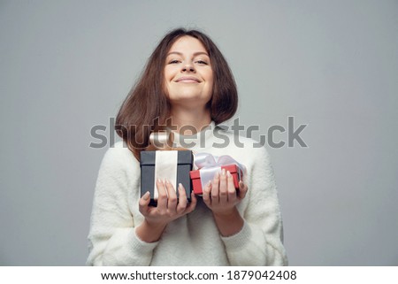 he holds boxes with gifts for the holiday. a young woman of Caucasian appearance stands in a gray background for the photo. Clothing white fluffy warm stylish jacket.