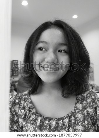 A happy asian teenage girl with floral patterns dress inside a bright bedroom, smiling. Black and white photo. 