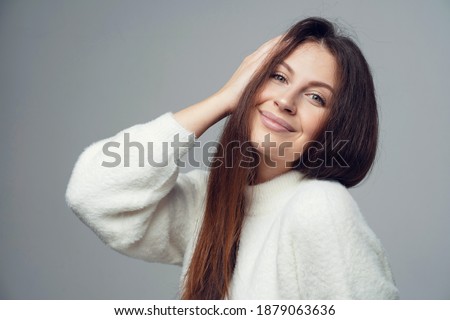 for photos of the hand touching the hair around the face portrait of smiling young brunette woman of Caucasian appearance. looking at the camera, posing in a photo studio on a gray background.