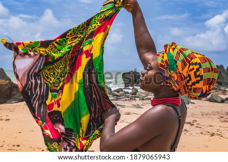 Dancing Ghana woman on the beautiful beach of Axim, located in Ghana West Africa. Headdress in traditional colors from Africa. Royalty-Free Stock Photo #1879065943