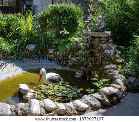 Artificial living area. Pond, water, stork, stones on the background of the bush. A good place for psychological relief.