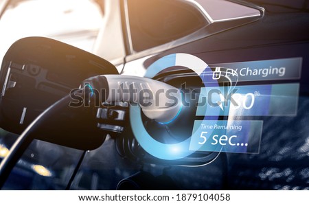 Power cable pump plug in charging power to electric vehicle EV car with modern technology UI control information display, car fueling station connected power cable alternative sustainable eco energy Royalty-Free Stock Photo #1879104058