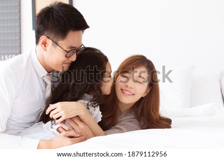 Happy Asian family spending a time together in bedroom, dad and mom cheering their playful daughter. Asian little girl enjoy playing in the bedroom with her father and mother. Happy family concept.
