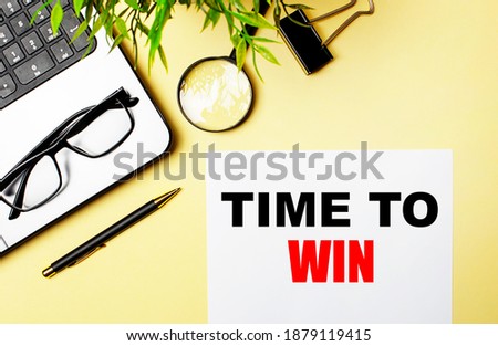 TIME TO WIN is written in red on a white piece of paper on a light yellow background next to a laptop, pen, magnifying glass, glasses and a green plant.
