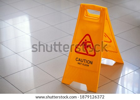 Selective focus. Yellow sign with the words Caution Wet Floor on the white tiled floor in the hotel. The concept of cleaning, cleaning service, hotel, security measures