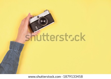 Composition in gray and yellow colors, color of the year 2021 - female hand holding old retro photo camera on yellow background with copy space. Online photography school concept. Selective focus