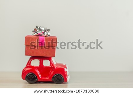 A red retro toy car delivers a gift box for a holiday on a light background.