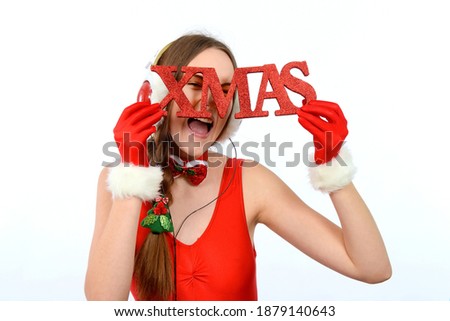 A young girl dresses up in red and wants to hear 
Christmas music. She wears headphones on her 
head and looks through a red glittering Xmas sign.