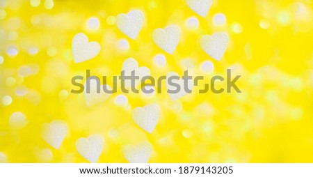 yellow background with bokeh of white foam hearts and light from a garland in partial blur, background of white hearts