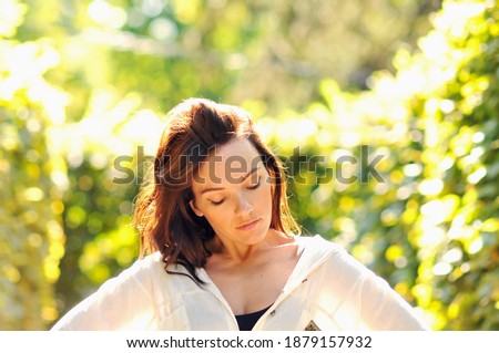 Portrait of a girl who poses in the park. A bright spot shines 
behind her back, beautiful bushes grow around, which create a blurred frame in the photo.
