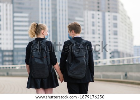 Schoolchildren, boy and girl in medical masks walk in the city.