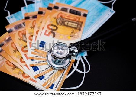 Medical stethoscope on Fifty euros banknotes and Medical Surgical Face Mask on Black background. Metaphor for expensive medicine and financial health. Concept of damage caused by coronavirus pandemic