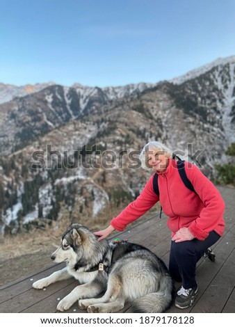 A cute elderly blonde woman in a pink sweater and a Alaskan Malamute in the Tien Shan mountains, Almaty