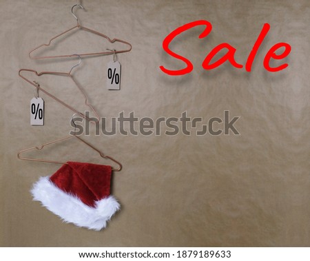 Christmas Santa Claus hat, empty hangers and discount price tags against a textured brown wall background. Sale, concept of christmas discounts and sales, copy space.