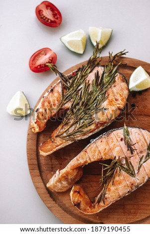 trout fish, cooked on a grill with rosemary, lies on a wooden cutting board. On the table next to tomatoes and lime. A soft picture. The view from the top.
