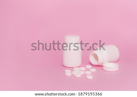 Two unmarked white medicine bottles and scattered pills on a pink background