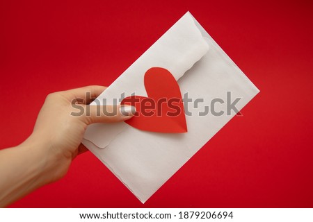 Woman's Hand holding envelope sealed with love in shape of red valentine's heart on red background. Valentine's Day