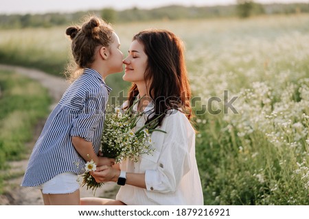 Daughter Kissing Mother and Give Flowers Bouquet. Little Girl Kiss Young Woman Nose Giving Chamomiles Present. Family Love and Funny Leisure Time Countryside Landscape. Nature Field on Background