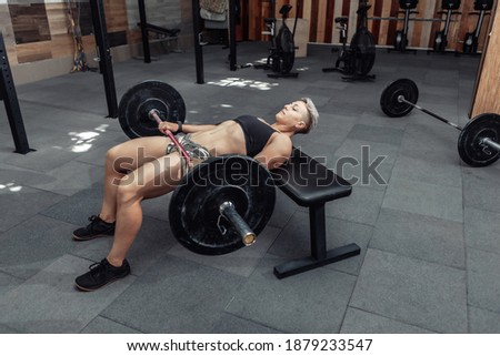 Young athletic strong woman practicing glute bridge exercise with a heavy barbell on her legs. Bodybuilding and Fitness Royalty-Free Stock Photo #1879233547