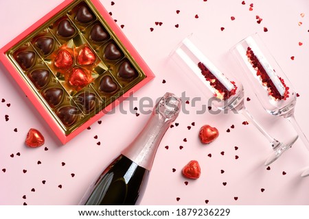 Valentines day greeting card with champagne glasses, bottle, candy hearts on pink background with confetti. Flat lay, view from above.