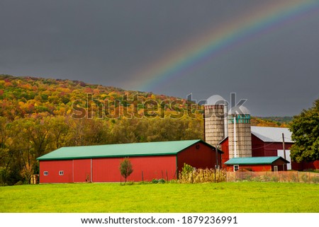A Red Barn and Silo in front of a hill with hardwood trees showing autumn fall colors in the Finger Lakes Region of Upper New York