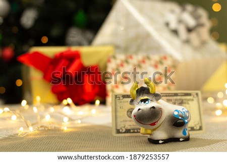 Cute cow figurine with 5 dollar bill, gifts and bright lights on blurred background, 2021 New Year bull symbol
