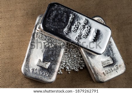 A silver bar and a pile of silver grains on the background to the coarse texture of the textile. Royalty-Free Stock Photo #1879262791