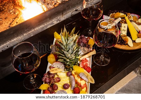 Cheese and fruit plate on the table by the fireplace. A sumptuous feast of fresh fruits and veggies, rustic breads, cheese and wine in the glass on a table in a rustic setting.