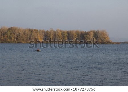 Autumn landscape with quiet river and lonely fisherman on the boat,colorful forest on island on background,relaxing place,holiday hobby,mans life,active lifestyle,october morning nature