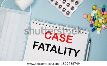 CASE FATALITY is written in a notebook on a blue background next to pills, mask and pen.