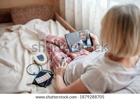 Old woman in bed looking at screen of laptop and consulting with a doctor online at home, telehealth services during lockdown, distant video call, modern tech healthcare application Royalty-Free Stock Photo #1879288705