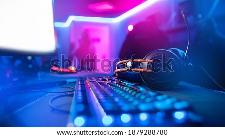 Professional headphones with microphone for video games and cyber sports gaming monitor in neon color blur background.