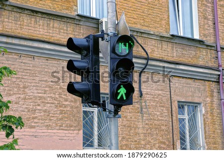 one black traffic light with a green signal on a gray pole on the street against a brown brick wall with windows